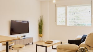 Uma sala de estar moderna com televisão de tela plana, piso de madeira, sofá, mesa de centro e uma pequena mesa redonda com um globo.