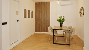 Uma área de refeições com uma mesa de madeira, quatro cadeiras, um vaso de planta e um ar-condicionado fixado na parede.