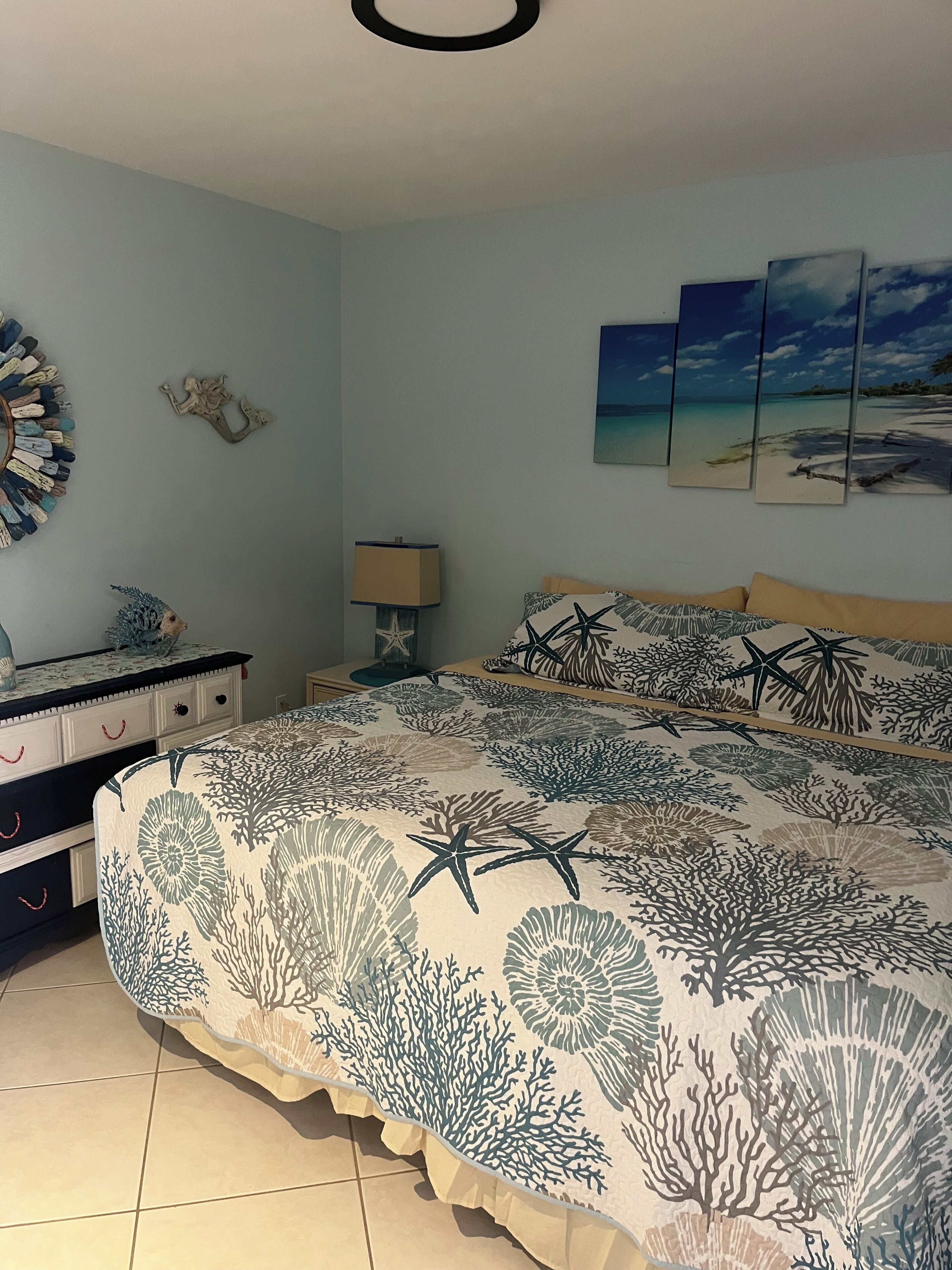 A bedroom with a bed, a dresser, a nightstand, a lamp, and a wall with three framed pictures.