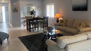 A living room with a sofa, coffee table, rug, and a dining area with chairs and a table. - Walk to Beach! Private Heated 3 bedroom Pool Home (Naples)