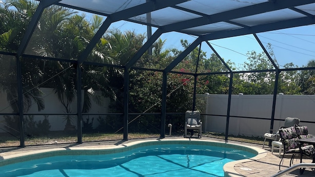 A swimming pool with a glass enclosure, surrounded by patio furniture and a white fence. - Walk to Beach! Private Heated 3 bedroom Pool Home (Naples)