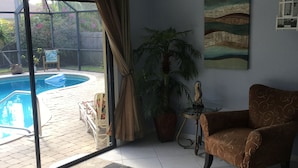 A living room with a pool, a chair, a table, and a painting. - Walk to Beach! Private Heated 3 bedroom Pool Home (Naples)