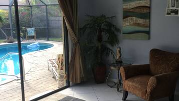 A living room with a pool, a chair, a table, and a painting.