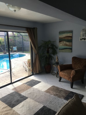 A living room with a pool, a chair, a table, and a painting. - Walk to Beach! Private Heated 3 bedroom Pool Home (Naples)