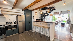 Una cocina moderna con una isla central, taburetes de bar y una escalera que sube a un nivel superior.