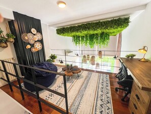 Ein modernes Loft mit hohen Decken, einer hängenden Grünpflanze, einem Holztisch, einem blauen Sitzsack und einem gemusterten Teppich.