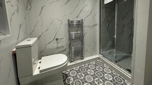 Casa de banho moderna com sanita, cabine de duche em vidro e chão estampado.