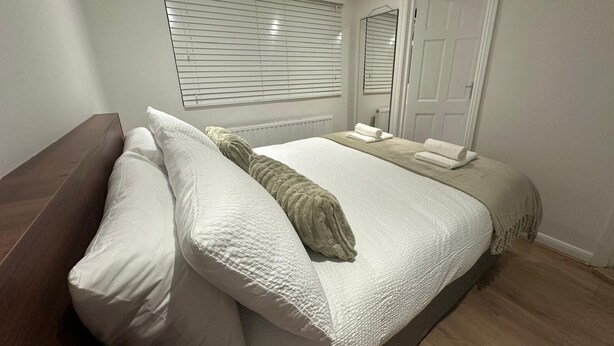 Quarto com cama, travesseiros, cobertor, mesa de cabeceira, espelho e porta.
