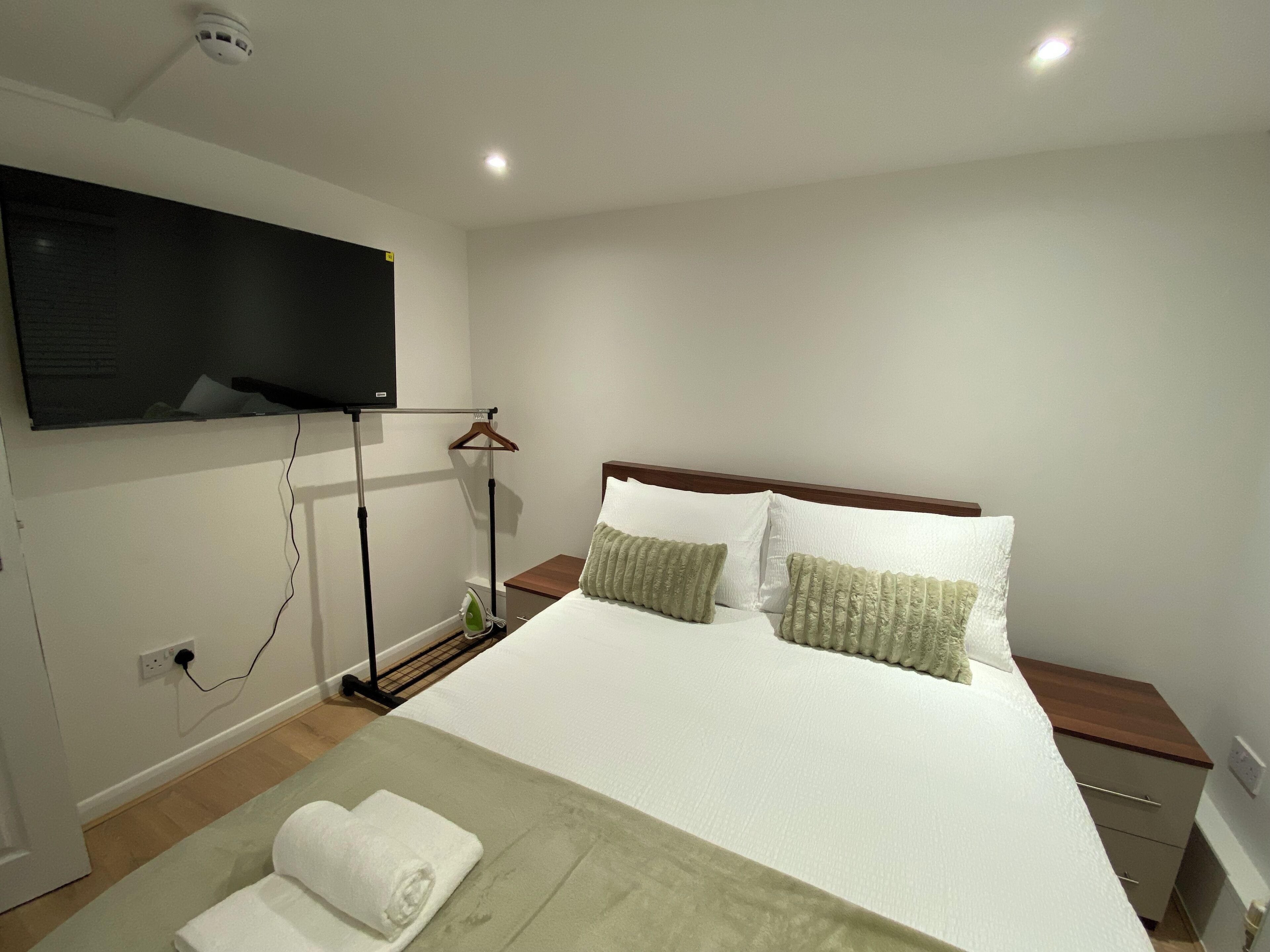 A bedroom with a bed, a flat-screen TV mounted on the wall, a bedside table, and a nightstand.