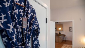 Quarto com piso xadrez, uma porta branca e uma área de cozinha ao fundo.