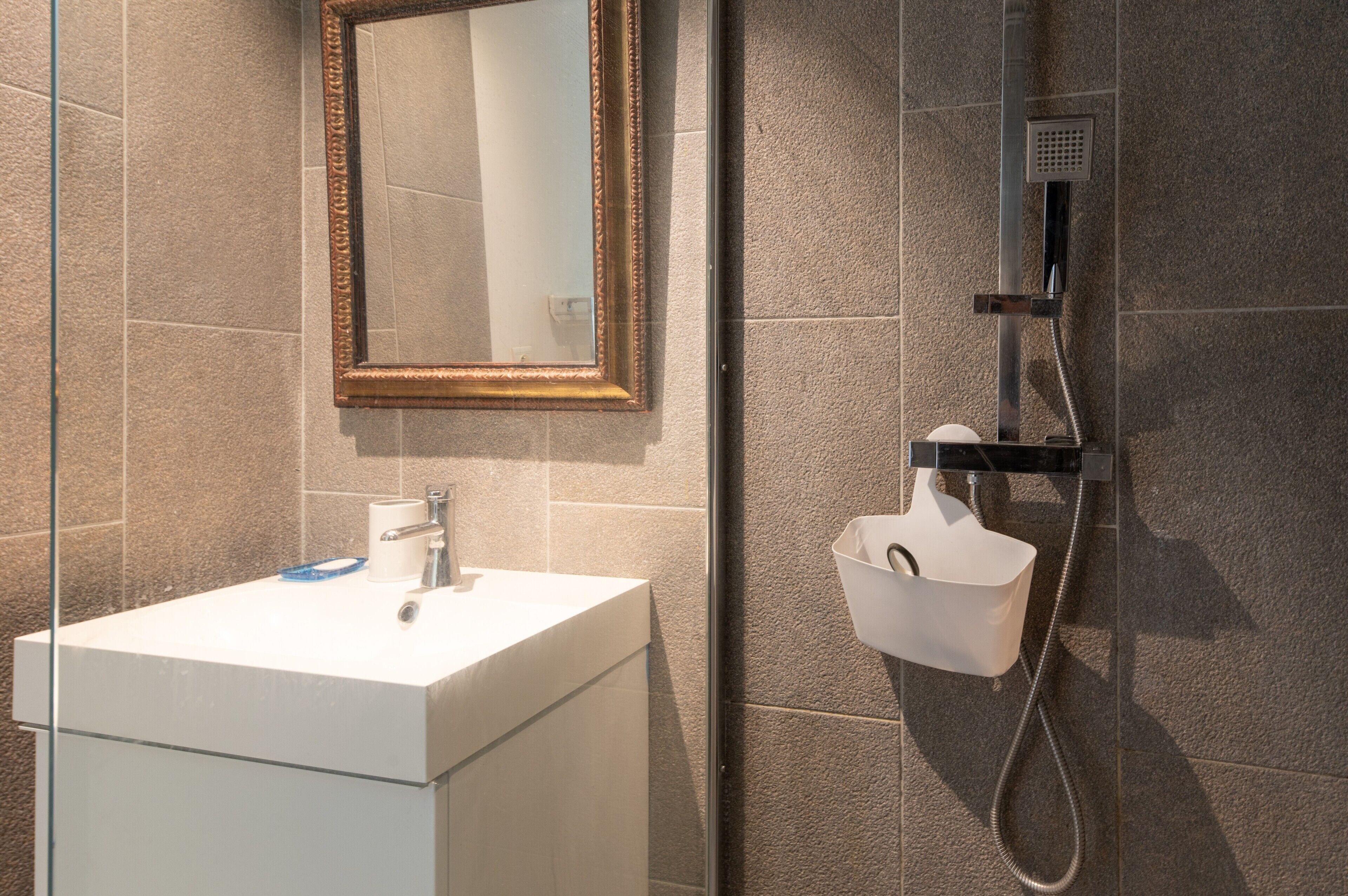 A bathroom with a white sink, a mirror with a gold frame, and a shower with a handheld showerhead.