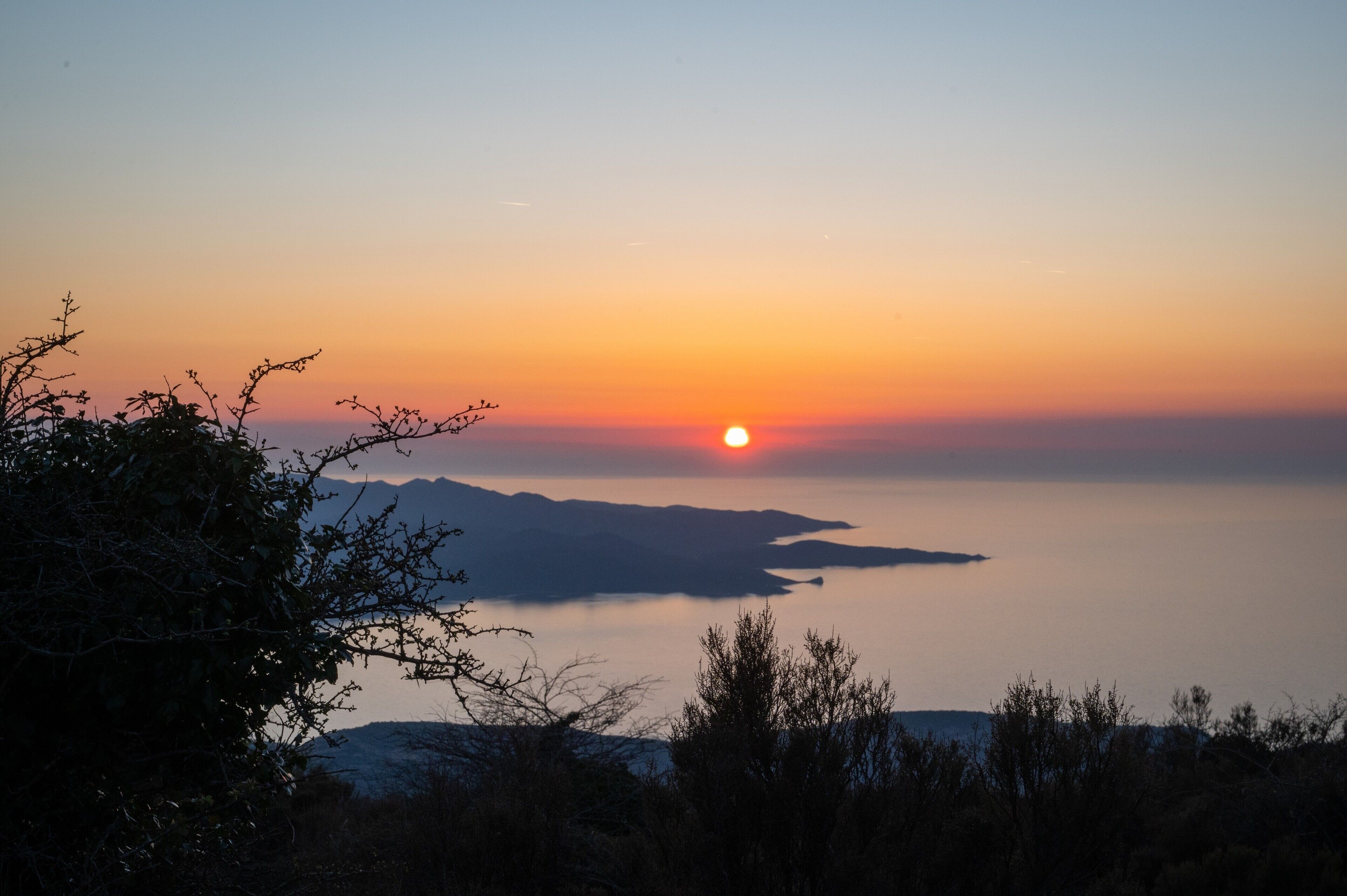 A sunset over a calm body of water with distant landforms.