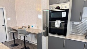 Een moderne keuken met een inbouwoven, een bar met krukken en grijze keukenkastjes.