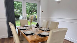 Een eetkamer met een houten tafel voor zes personen, omringd door beige stoelen, met uitzicht op groen buiten.