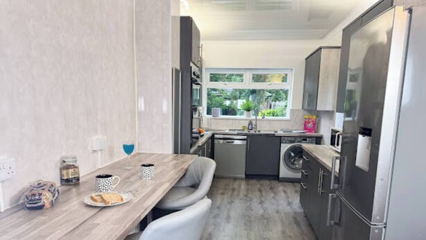 Een kleine keuken met een houten tafel, stoelen, een wasmachine en een koelkast.