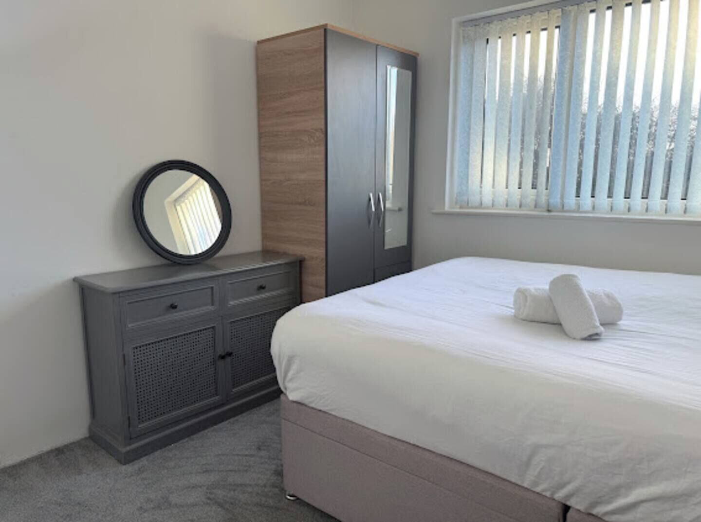 A bedroom with a bed, a wardrobe, a mirror, and a window with blinds.