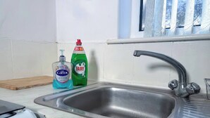 Uma cozinha com uma pia de aço inoxidável, uma tábua de corte e duas garrafas de detergente.
