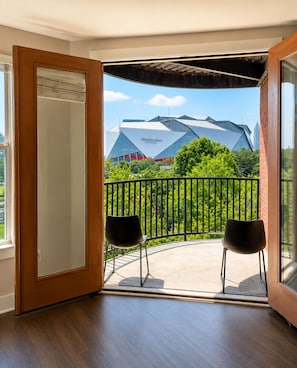 An open door leading to a balcony with two chairs, a view of a stadium, and a brick wall. - Downtown Atlanta Loft, 1 Block to Mercedes-Benz Stadium, FREE Parking (Atlanta)