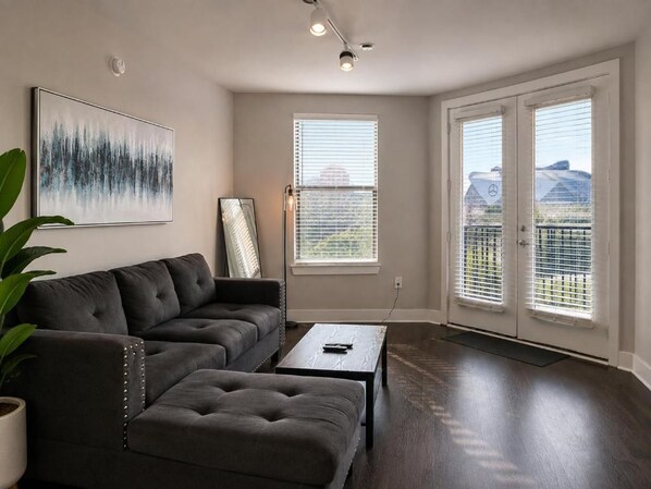 A living room with a sectional sofa, a coffee table, and a painting on the wall. - Downtown Atlanta Loft, 1 Block to Mercedes-Benz Stadium, FREE Parking (Atlanta)