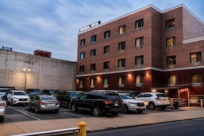 A multi-story hotel with a brick facade, multiple windows, and a parking lot with various cars. - Imperial Hotel (Brooklyn)