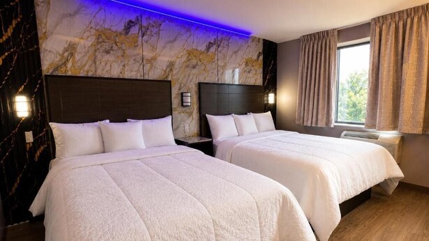 A hotel room with two beds, marble wall, and a window with curtains. - Imperial Hotel (Brooklyn)