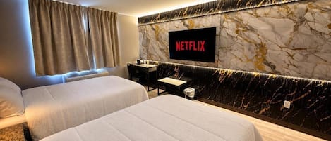 Habitación de hotel con dos camas, un televisor montado en una pared de mármol y una mesita de noche con una lámpara.