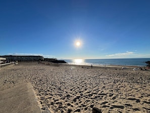 A beach with a clear sky, the sun low on the horizon, and a building with a sign in the background. - Studio with terrace, 200m from the beach (Anglet)