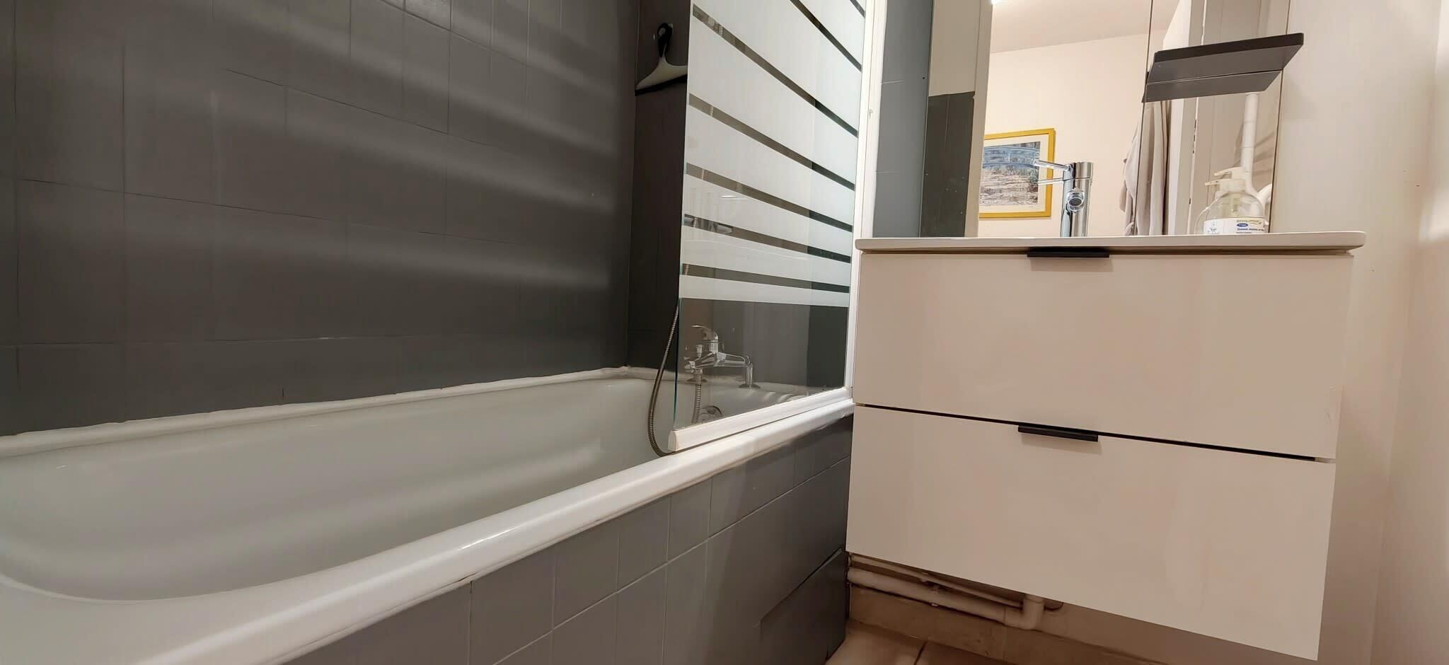Une salle de bain avec une baignoire, un miroir et un meuble blanc.