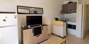 A compact kitchen with a built-in oven, microwave, and a small dining area with a wooden table. - Studio with Balcony, Pool & Parking. (Fréjus)