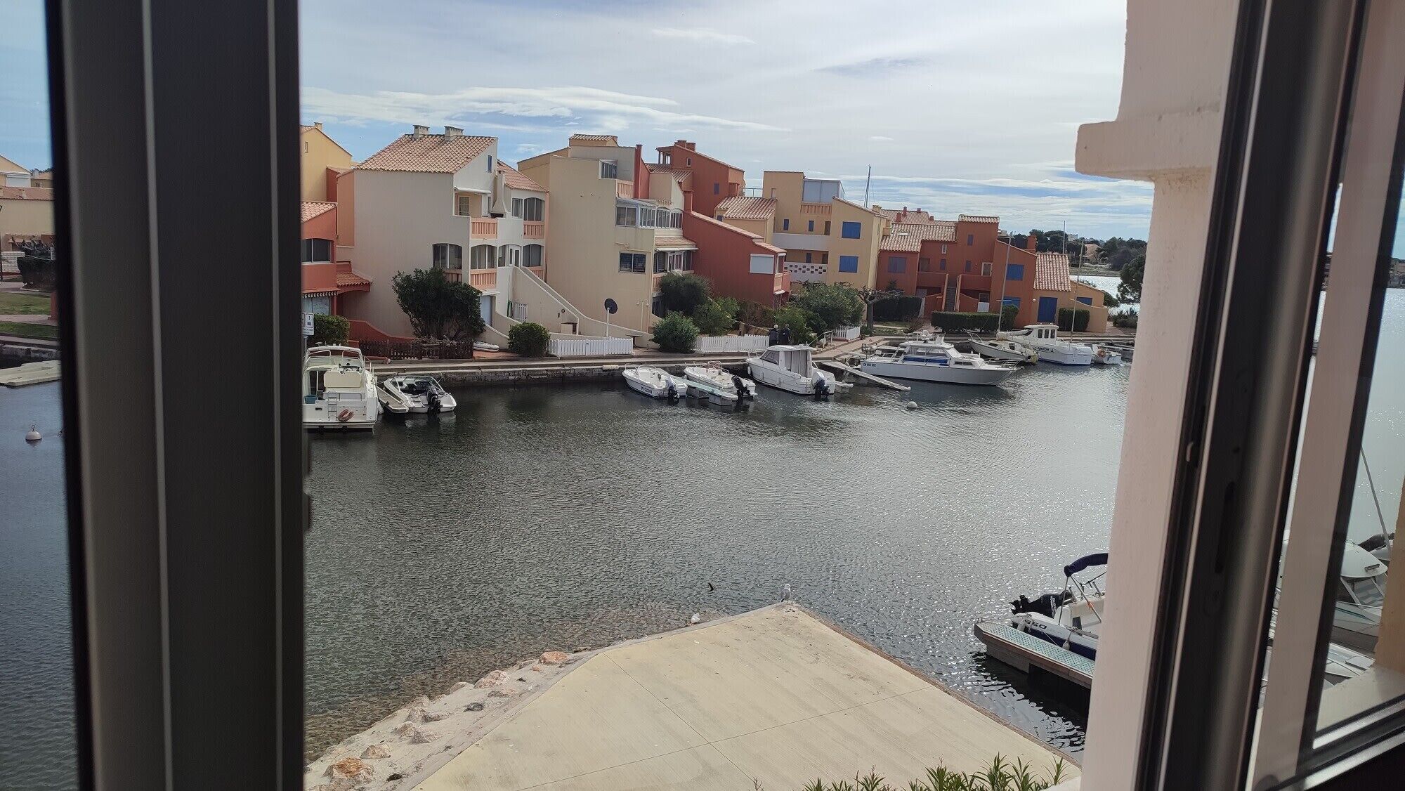 Un port de plaisance avec des bateaux amarrés, une étendue d’eau calme et, au loin, des bâtiments dotés de balcons.