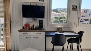 Quarto com televisão, máquina de café, chaleira, tigela e duas cadeiras.