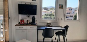 A room with a TV, a coffee maker, a kettle, a bowl, and two chairs. - Bright studio, 300m from beach with balcony (Fréjus)