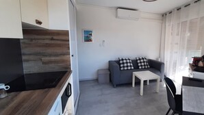 Um espaço compacto para viver com cozinha americana, sofá cinza com almofadas xadrez, uma mesa pequena e uma TV em uma prateleira.