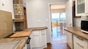 A kitchen with white cabinets, a wooden countertop, and a view of the sea through an open door. - Apartment with Panoramic Sea View (Ajaccio)