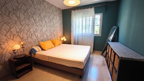 A bedroom with a bed, bedside lamps, a nightstand, a mirror, and a window with curtains. - Apartment with Panoramic Sea View (Ajaccio)