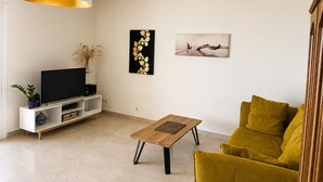 A living room with a sofa, a coffee table, a TV, and artwork on the wall. - Apartment with Panoramic Sea View (Ajaccio)