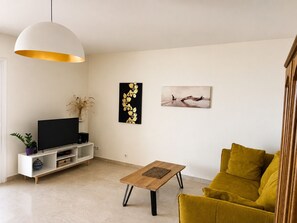 A living room with a sofa, a coffee table, a TV, and artwork on the wall. - Apartment with Panoramic Sea View (Ajaccio)