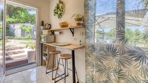 A kitchen with a sliding door to a balcony, a wooden countertop, stools, and a hanging wreath. - Les Vignes Guest Room with Private Entrance, Wi-Fi, and Air Conditioning (Puisserguier)