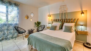 A bedroom with a bed, two chairs, a nightstand, a wall-mounted mirror, and a ceiling fan. - Les Vignes Guest Room with Private Entrance, Wi-Fi, and Air Conditioning (Puisserguier)