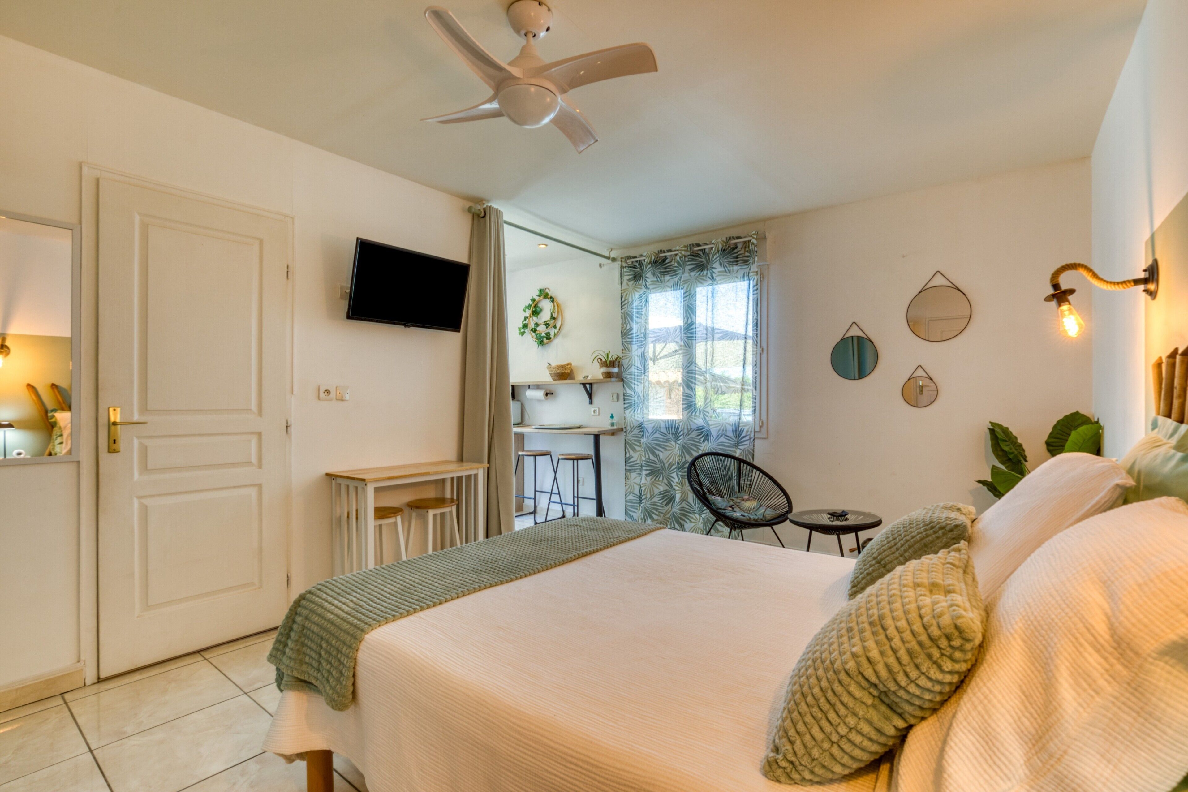 Un dormitorio con cama, ventilador de techo, televisor, escritorio y ventana con cortinas.