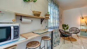 A kitchen with a microwave, wooden bar stool, and a shelf with baskets. - Les Vignes Guest Room with Private Entrance, Wi-Fi, and Air Conditioning (Puisserguier)