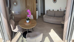 Ein modernes Wohnzimmer mit einem runden Holztisch, zwei Stühlen, einem Sofa und einer dekorativen Orchideenpflanze.