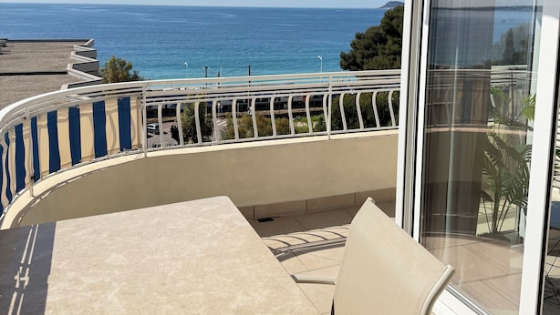 Ein Balkon mit Tisch und Stühlen, Blick auf das Meer, und ein Gebäude mit gestreifter Markise.