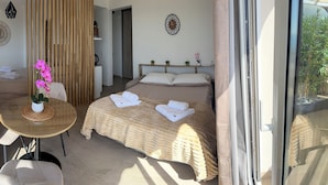Ein Zimmer mit einem Bett, einem Tisch mit Topfpflanze, einem Stuhl und einem Fenster.
