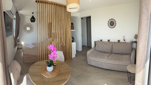 Ein modernes Wohnzimmer mit einer Couch, einem runden Holztisch mit Orchidee im Topf, einer Wanduhr und einem Holzverkleidungselement.