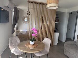 A modern hotel room with a bed, a dining table with chairs, a potted orchid, and a hanging light fixture. - BEAUTIFUL STUDIO SLEEPS 4 SEA VIEW CANNES (Cannes)