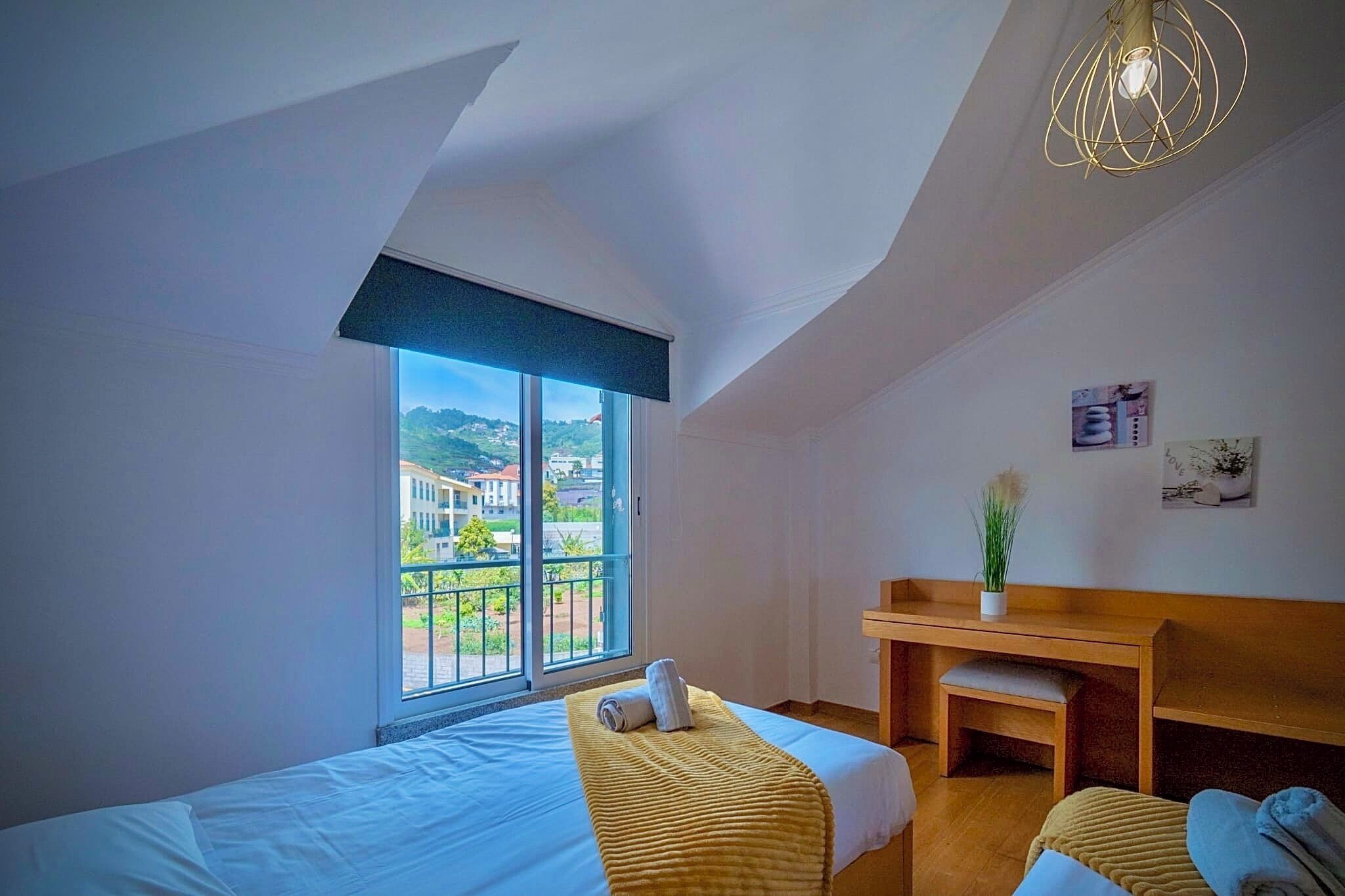 A hotel room with two beds, a desk, a view of the outside, and a ceiling light fixture.