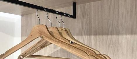 A wooden hanger with a black metal bracket against a light wooden wall.