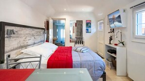 Una habitación de hotel moderna con una cama, un escritorio, un televisor y un baño visible a través de una puerta abierta.