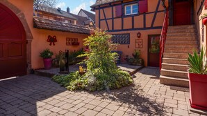 Un patio con un árbol en el centro, una puerta roja y un edificio de fachada entramada.
